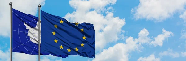 Antártida y la bandera de la Unión Europea ondeando en el viento contra el cielo azul nublado blanco juntos. Concepto diplomático, relaciones internacionales . — Foto de Stock