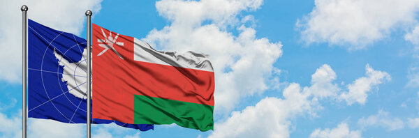 Antarctica and Oman flag waving in the wind against white cloudy blue sky together. Diplomacy concept, international relations.