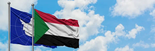 Bandera de la Antártida y Sudán ondeando en el viento contra el cielo azul nublado blanco juntos. Concepto diplomático, relaciones internacionales . — Foto de Stock
