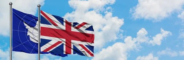 Antarktis och Storbritannien flagga vifta i vinden mot vit grumlig blå himmel tillsammans. Diplomatisk koncept, internationella relationer. — Stockfoto