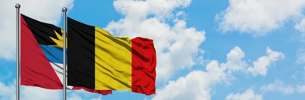 Antigua y Barbuda con la bandera de Bélgica ondeando en el viento contra el cielo azul nublado blanco juntos. Concepto diplomático, relaciones internacionales . — Foto de Stock