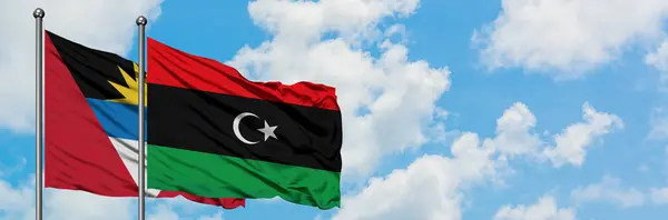 Antigua y Barbuda con la bandera de Libia ondeando en el viento contra el cielo azul nublado blanco juntos. Concepto diplomático, relaciones internacionales . — Foto de Stock