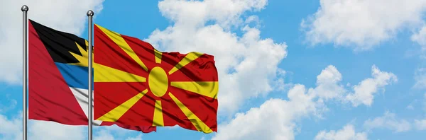 Antigua și Barbuda cu steagul Macedoniei fluturând în vânt împotriva cerului albastru și noros alb împreună. Conceptul de diplomație, relațiile internaționale . — Fotografie, imagine de stoc