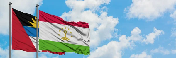 Antigua y Barbuda con la bandera de Tayikistán ondeando en el viento contra el cielo azul nublado blanco juntos. Concepto diplomático, relaciones internacionales . — Foto de Stock
