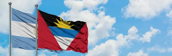 Argentina och Antigua och Barbuda flagga vifta i vinden mot vit grumlig blå himmel tillsammans. Diplomatisk koncept, internationella relationer. — Stockfoto