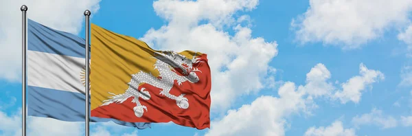 Bandera de Argentina y Bután ondeando en el viento contra el blanco cielo azul nublado juntos. Concepto diplomático, relaciones internacionales . — Foto de Stock