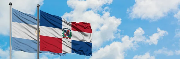 Bandeira da Argentina e República Dominicana agitando no vento contra o céu azul nublado branco juntos. Conceito de diplomacia, relações internacionais . — Fotografia de Stock