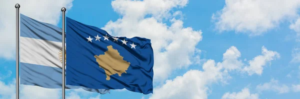 Bandera de Argentina y Kosovo ondeando en el viento contra el cielo azul nublado blanco juntos. Concepto diplomático, relaciones internacionales . — Foto de Stock