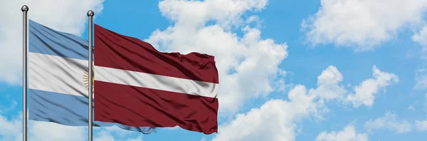 Argentina och Lettland flagga vifta i vinden mot vit grumlig blå himmel tillsammans. Diplomatisk koncept, internationella relationer. — Stockfoto