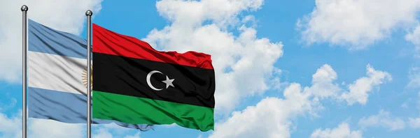 Bandera de Argentina y Libia ondeando en el viento contra el cielo azul nublado blanco juntos. Concepto diplomático, relaciones internacionales . — Foto de Stock