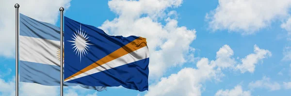 Bandera de Argentina e Islas Marshall ondeando en el viento contra el cielo azul nublado blanco juntos. Concepto diplomático, relaciones internacionales . — Foto de Stock