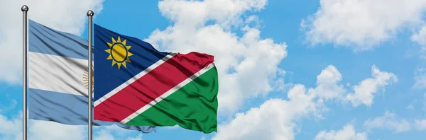 Bandera de Argentina y Namibia ondeando en el viento contra el cielo azul nublado blanco juntos. Concepto diplomático, relaciones internacionales . — Foto de Stock