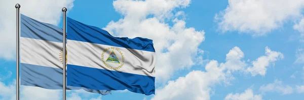 Argentinien und Nicaragua schwenken gemeinsam die Flagge im Wind vor dem wolkenverhangenen blauen Himmel. Diplomatie-Konzept, internationale Beziehungen. — Stockfoto