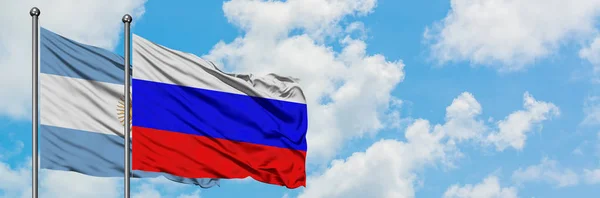 Argentiniens und Russlands Flagge weht gemeinsam im Wind gegen den wolkenverhangenen blauen Himmel. Diplomatie-Konzept, internationale Beziehungen. — Stockfoto