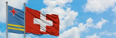 Aruba ve İsviçre bayrağı birlikte beyaz bulutlu mavi gökyüzüne karşı rüzgarda sallayarak. Diplomasi kavramı, uluslararası ilişkiler.