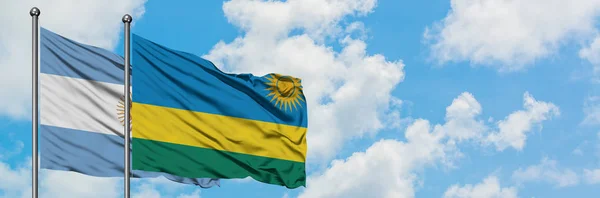 Bandera de Argentina y Ruanda ondeando en el viento contra el cielo azul nublado blanco juntos. Concepto diplomático, relaciones internacionales . — Foto de Stock