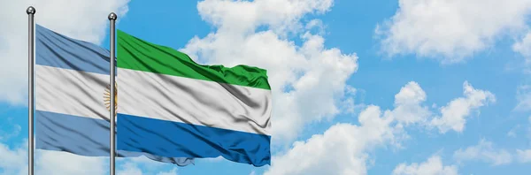 Bandera de Argentina y Sierra Leona ondeando en el viento contra el cielo azul nublado blanco juntos. Concepto diplomático, relaciones internacionales . — Foto de Stock