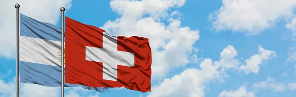 Argentyna i Szwajcaria flaga machając w wiatr przed białym zachmurzone błękitne niebo razem. Koncepcja dyplomacji, stosunki międzynarodowe. — Zdjęcie stockowe