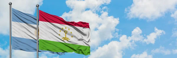 Bandera de Argentina y Tayikistán ondeando en el viento contra el cielo azul nublado blanco juntos. Concepto diplomático, relaciones internacionales . — Foto de Stock