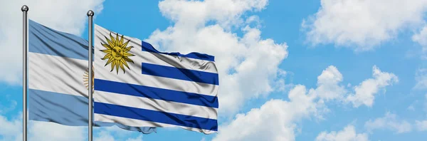 Bandeira da Argentina e do Uruguai agitando no vento contra o céu azul nublado branco juntos. Conceito de diplomacia, relações internacionais . — Fotografia de Stock