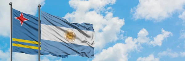 Aruba e a bandeira da Argentina agitando no vento contra o céu azul nublado branco juntos. Conceito de diplomacia, relações internacionais . — Fotografia de Stock