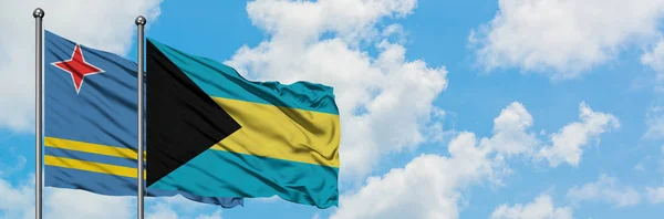 Aruba a Bahamské vlajky ve větru mávali proti bíle zatažené modré obloze. Diplomacie, mezinárodní vztahy. — Stock fotografie