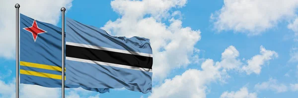 Aruba e la bandiera del Botswana sventolano insieme nel vento contro il bianco cielo blu nuvoloso. Concetto di diplomazia, relazioni internazionali . — Foto Stock