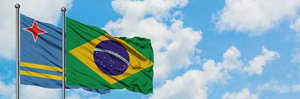 Bandera de Aruba y Brasil ondeando en el viento contra el cielo azul nublado blanco juntos. Concepto diplomático, relaciones internacionales . — Foto de Stock