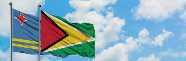 Aruba e a bandeira da Guiana agitando no vento contra o céu azul nublado branco juntos. Conceito de diplomacia, relações internacionais . — Fotografia de Stock