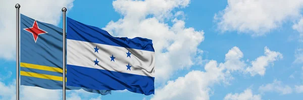 Bandera de Aruba y Honduras ondeando en el viento contra el cielo azul nublado blanco juntos. Concepto diplomático, relaciones internacionales . — Foto de Stock