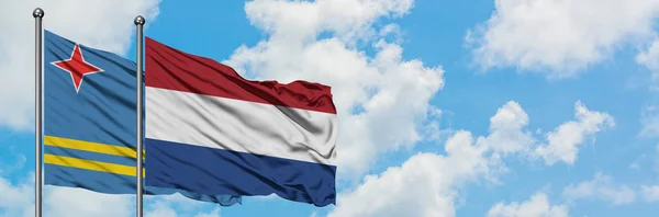 Aruba e la bandiera olandese sventolano insieme nel vento contro il bianco cielo blu nuvoloso. Concetto di diplomazia, relazioni internazionali . — Foto Stock