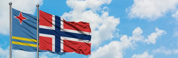 Bandera de Aruba y Noruega ondeando en el viento contra el cielo azul nublado blanco juntos. Concepto diplomático, relaciones internacionales . — Foto de Stock