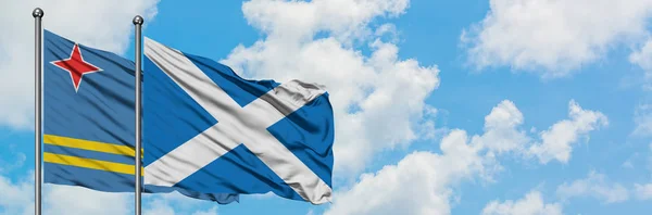 Bandera de Aruba y Escocia ondeando en el viento contra el cielo azul nublado blanco juntos. Concepto diplomático, relaciones internacionales . — Foto de Stock