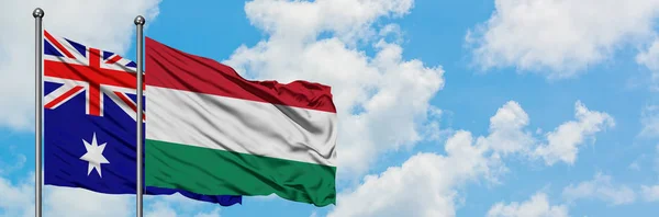 Bandera de Australia y Hungría ondeando en el viento contra el cielo azul nublado blanco juntos. Concepto diplomático, relaciones internacionales . — Foto de Stock