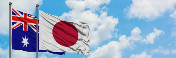 Bandera de Australia y Japón ondeando en el viento contra el cielo azul nublado blanco juntos. Concepto diplomático, relaciones internacionales . —  Fotos de Stock