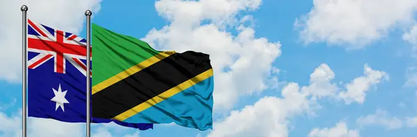 Bandera de Australia y Tanzania ondeando en el viento contra el cielo azul nublado blanco juntos. Concepto diplomático, relaciones internacionales . — Foto de Stock