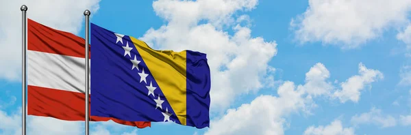 Bandera de Austria y Bosnia Herzegovina ondeando en el viento contra el cielo azul nublado blanco juntos. Concepto diplomático, relaciones internacionales . — Foto de Stock