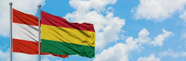 Bandera de Austria y Bolivia ondeando en el viento contra el cielo azul nublado blanco juntos. Concepto diplomático, relaciones internacionales . — Foto de Stock
