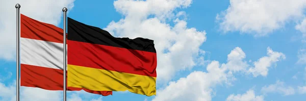 Österreich und Deutschland wehen gemeinsam im Wind vor dem wolkenverhangenen blauen Himmel. Diplomatie-Konzept, internationale Beziehungen. — Stockfoto