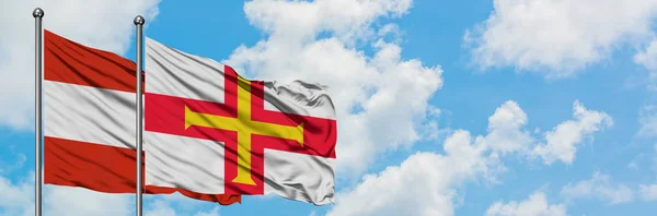 Bandera de Austria y Guernsey ondeando en el viento contra el cielo azul nublado blanco juntos. Concepto diplomático, relaciones internacionales . — Foto de Stock