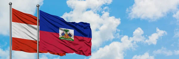 一緒に白い曇り青い空に対して風に手を振るオーストリアとハイチの旗。外交概念、国際関係. — ストック写真