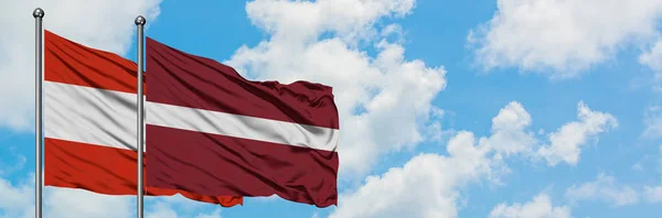 Österrike och Lettland flagga vifta i vinden mot vit grumlig blå himmel tillsammans. Diplomatisk koncept, internationella relationer. — Stockfoto