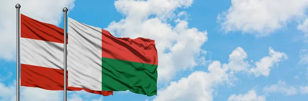 Bandera de Austria y Madagascar ondeando en el viento contra el cielo azul nublado blanco juntos. Concepto diplomático, relaciones internacionales . — Foto de Stock