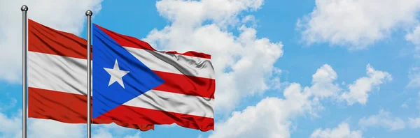 Österreich und Puerto Rico wehen gemeinsam im Wind vor dem wolkenverhangenen blauen Himmel. Diplomatie-Konzept, internationale Beziehungen. — Stockfoto