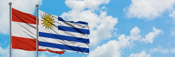 Bandera de Austria y Uruguay ondeando en el viento contra el cielo azul nublado blanco juntos. Concepto diplomático, relaciones internacionales . —  Fotos de Stock