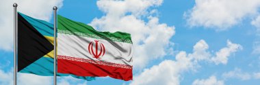 Bahamalar ve İran bayrağı birlikte beyaz bulutlu mavi gökyüzüne karşı rüzgarda sallayarak. Diplomasi kavramı, uluslararası ilişkiler.