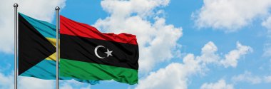 Bahamalar ve Libya bayrağı birlikte beyaz bulutlu mavi gökyüzüne karşı rüzgarda sallayarak. Diplomasi kavramı, uluslararası ilişkiler.
