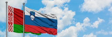Beyaz Rusya ve Slovenya bayrağı birlikte beyaz bulutlu mavi gökyüzüne karşı rüzgarda sallayarak. Diplomasi kavramı, uluslararası ilişkiler.