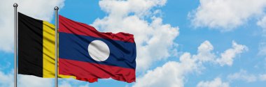 Belçika ve Laos bayrağı birlikte beyaz bulutlu mavi gökyüzüne karşı rüzgarda sallayarak. Diplomasi kavramı, uluslararası ilişkiler.