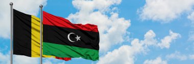 Belçika ve Libya bayrağı birlikte beyaz bulutlu mavi gökyüzüne karşı rüzgarsal sallayarak. Diplomasi kavramı, uluslararası ilişkiler.